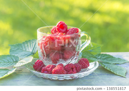 Red raspberries in a transparent tea cup on a table against green natural background 138551817