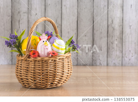 Happy easter holidays greeting card template; wicker basket with easter eggs and flowers on a wooden table against wooden background; copy space 138553075