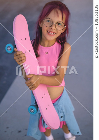 A beautiful funny girl with dyed pink hair holds a skateboard in hands. A beautiful funny girl with dyed pink hair holds a skateboard in hands. 138553138