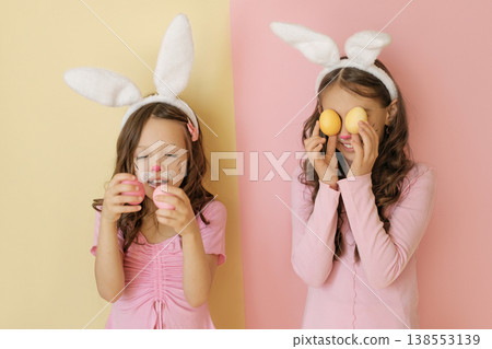 Funny girls are playing with colored Easter eggs dressed up as Rabbits. Children in the guise of the Easter bunny Funny girls are playing with colored Easter eggs dressed up as Rabbits. Children in the guise of the Easter bunny 138553139