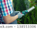 gardener trimming bush with electric shears in garden 138553306