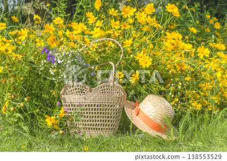 Summer leisure activities concept; Bouquet of wild flowers in a wicker bag  on a green lawn near blooming yellow flowers 138553529