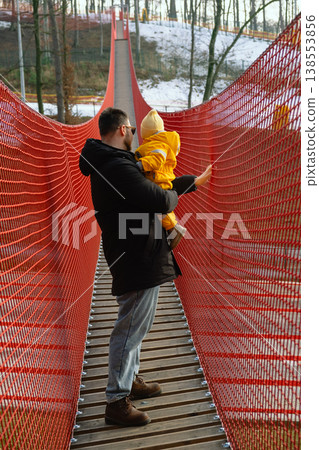 Father holding toddler on red suspension bridge in winter forest 138553856