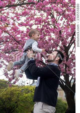 Father lifting baby under pink cherry blossoms in spring Father lifting baby under pink cherry blossoms in spring 138553880