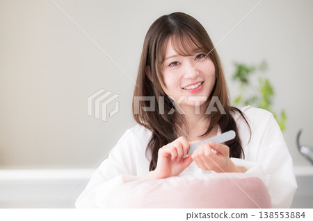 一位女性在家中進行指甲護理；用指甲銼磨指甲；一張展現女性美麗生活方式的圖片，畫面中女性直視鏡頭。 138553884