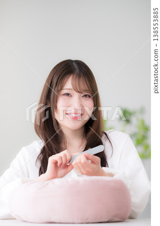 A woman doing self-nail care at home; polishing her nails with a nail file; a beauty lifestyle image of a woman looking directly at the camera. 138553885