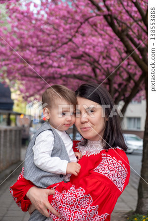 Smiling mother holding toddler under cherry blossom trees 138553888