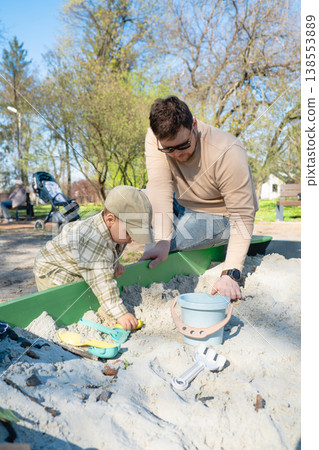 Father and son playing in sandbox outdoors on sunny day 138553889