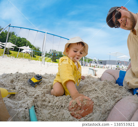 Father and toddler playing in sandbox at playground 138553921