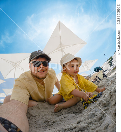 Father and toddler playing in sand under beach umbrellas 138553968