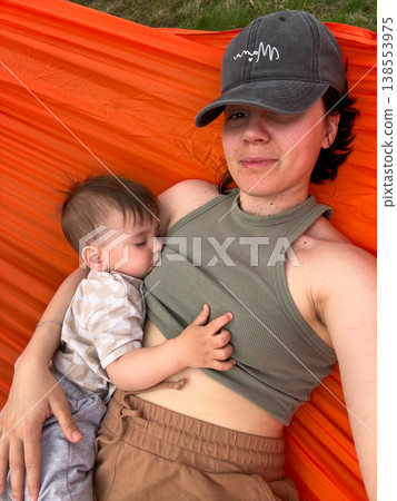 Mother and baby cuddling in orange hammock outdoors 138553975