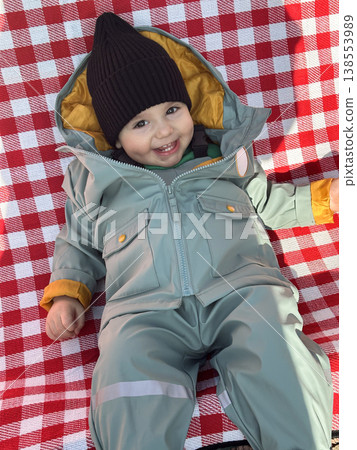 Smiling toddler in winter snowsuit on red checkered blanket 138553989