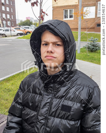 Adolescence clad in cozy street fashion. Youth with focused expression in cold city environment Adolescence clad in cozy street fashion. Youth with focused expression in cold city environment 138554637