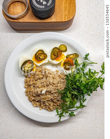 Rustic dish with peppers and herbs. Nutritious oatmeal entree and boiled eggs with chili and fresh greenery Rustic dish with peppers and herbs. Nutritious oatmeal entree and boiled eggs with chili and fresh greenery 138554645
