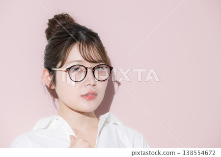 A cute and beautiful woman with a bun hairstyle and glasses (sunglasses) against a pink background, perfect for beauty and aesthetics images. 138554672