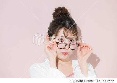 A cute and beautiful woman with a bun hairstyle and glasses (sunglasses) against a pink background, perfect for beauty and aesthetics images. A cute and beautiful woman with a bun hairstyle and glasses (sunglasses) against a pink background, perfect for beauty and aesthetics images. 138554676