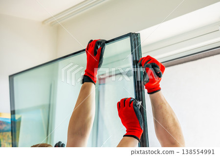 Worker separating triple glazed window glass unit into individual panels for safe handling and disposal after damage in apartment. Window repair, glass recycling and maintenance process concept. Worker separating triple glazed window glass unit into individual panels for safe handling and disposal after damage in apartment. Window repair, glass recycling and maintenance process concept. 138554991