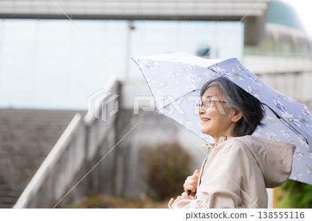 特寫鏡頭展現了一位平靜、健康、活躍的老人撐著傘在雨季散步。 138555116