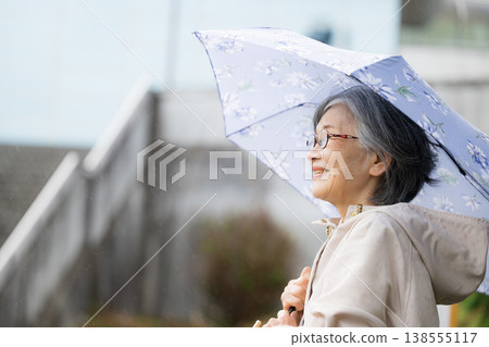 特寫鏡頭展現了一位平靜、健康、活躍的老人撐著傘在雨季散步。 138555117