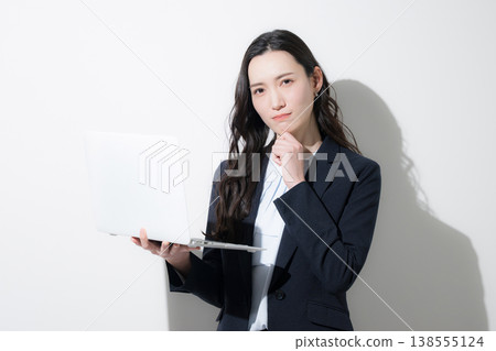 A cool, business-suited woman with her hand on her chin, holding a laptop, is shown against a white background, in a thoughtful, contemplative pose. (Image caption: Job hunting) A cool, business-suited woman with her hand on her chin, holding a laptop, is shown against a white background, in a thoughtful, contemplative pose. (Image caption: Job hunting) 138555124
