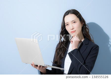 A cool, business-suited woman with her hand on her chin, holding a laptop, is shown against a light blue background, in a thoughtful, contemplative pose. (Image caption: Job hunting) A cool, business-suited woman with her hand on her chin, holding a laptop, is shown against a light blue background, in a thoughtful, contemplative pose. (Image caption: Job hunting) 138555126