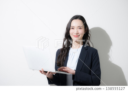 A stylish woman in a business suit holding a laptop against a white background, looking directly at the camera from the waist up, suggesting topics such as career changes, the future, and goals. A stylish woman in a business suit holding a laptop against a white background, looking directly at the camera from the waist up, suggesting topics such as career changes, the future, and goals. 138555127