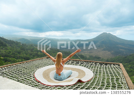 A person sits on a net overlooking the valley and mountains 138555276