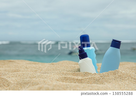 Sunscreen bottles sit in the sand near the ocean Sunscreen bottles sit in the sand near the ocean 138555288