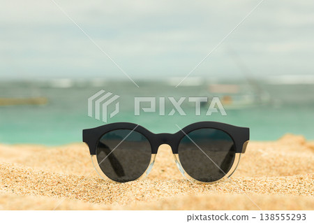 Sunglasses placed on sand with the ocean in background Sunglasses placed on sand with the ocean in background 138555293