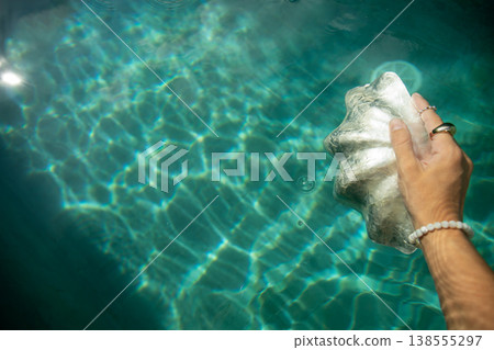 Hand holds shiny shell above clear blue water 138555297