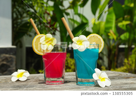 Two colorful drinks sit on a table with tropical flowers nearby Two colorful drinks sit on a table with tropical flowers nearby 138555305