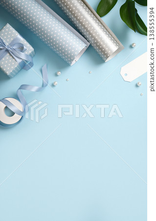 Gift wrapping with blue and silver wrapping paper, ribbon, scissors, and small gift boxes on blue backdrop. Copy space. Gift wrapping with blue and silver wrapping paper, ribbon, scissors, and small gift boxes on blue backdrop. Copy space. 138555394