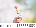 A hand holding a three-colored dango (rice dumpling). The image is one of "dumplings over flowers." 138555665