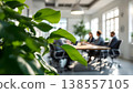Photo of business meeting in modern office with green plant in foreground, showcasing collaboration and corporate environment. Photo of business meeting in modern office with green plant in foreground, showcasing collaboration and corporate environment. 138557105