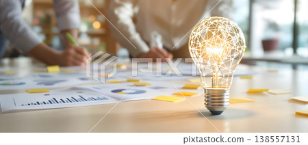 Photo of light bulb with network inside on a table with charts and people brainstorming, concept of innovation and teamwork 138557131