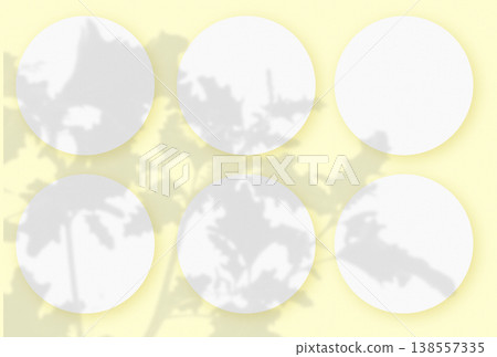 Natural light casts shadows from wild grasses on 6 round sheets of white textured paper lying on an yellow textured background. Mockup Natural light casts shadows from wild grasses on 6 round sheets of white textured paper lying on an yellow textured background. Mockup 138557335