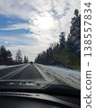Winter road through coniferous forest, view from car. Sunny day, blue sky with clouds and snowy roadsides 138557834