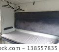 Interior of a modern train sleeping car. Comfortable passenger seat with soft upholstery, clothes hangers and clean bed 138557835