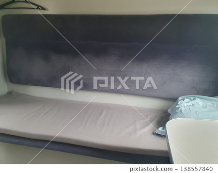 Interior of a modern train sleeping car. Comfortable passenger seat with soft upholstery, clothes hangers and clean bed Interior of a modern train sleeping car. Comfortable passenger seat with soft upholstery, clothes hangers and clean bed 138557840