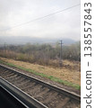View of railway tracks and foggy mountains from train window. Gloomy spring landscape, metal rails, telegraph poles 138557843