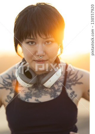 Young woman with headphones and tattoos standing outdoors 138557920