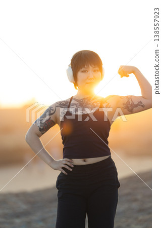 Confident woman flexing bicep at golden sunset Confident woman flexing bicep at golden sunset 138557923