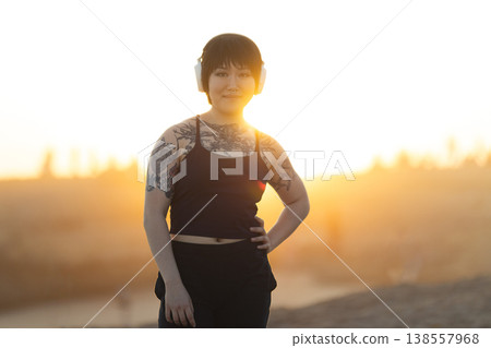 Young smiling tattooed person wearing headphones at sunset Young smiling tattooed person wearing headphones at sunset 138557968
