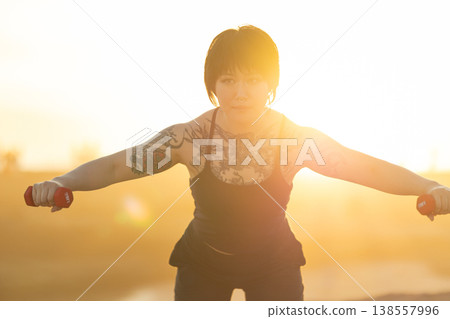 Woman lifting light dumbbells in outdoor fitness session Woman lifting light dumbbells in outdoor fitness session 138557996