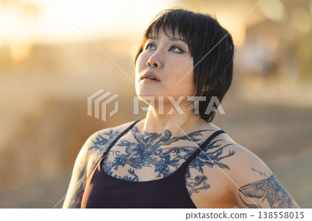 Young woman with tattoos looking up confidently Young woman with tattoos looking up confidently 138558015