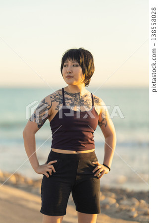 Strong tattooed young woman standing on beach having confidence Strong tattooed young woman standing on beach having confidence 138558028