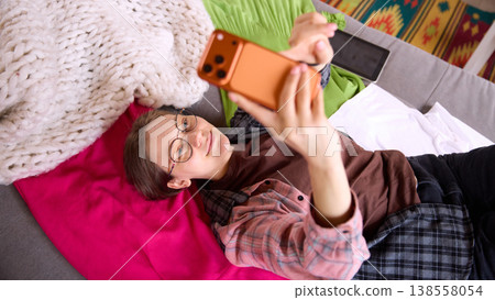 Woman lying on sofa taking selfie with smartphone at home. 138558054