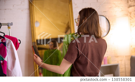 Woman trying clothes in front of mirror at home while using smartphone 138558301