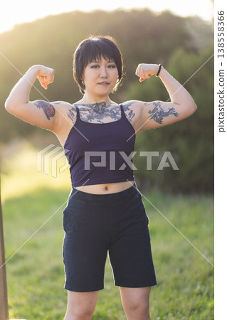 Tattooed woman flexing biceps showing strength and confidence 138558366