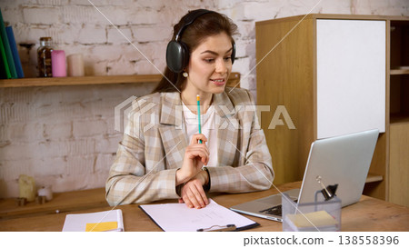 Young woman in headphones studying online with laptop at home desk. 138558396